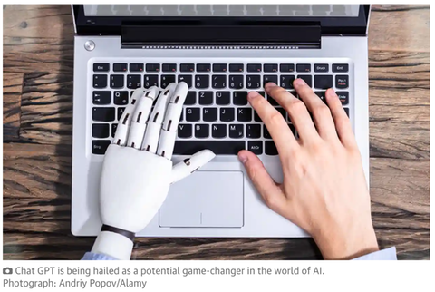 Photograph of a laptop keyboard with one human hand and one robot hand on it typing